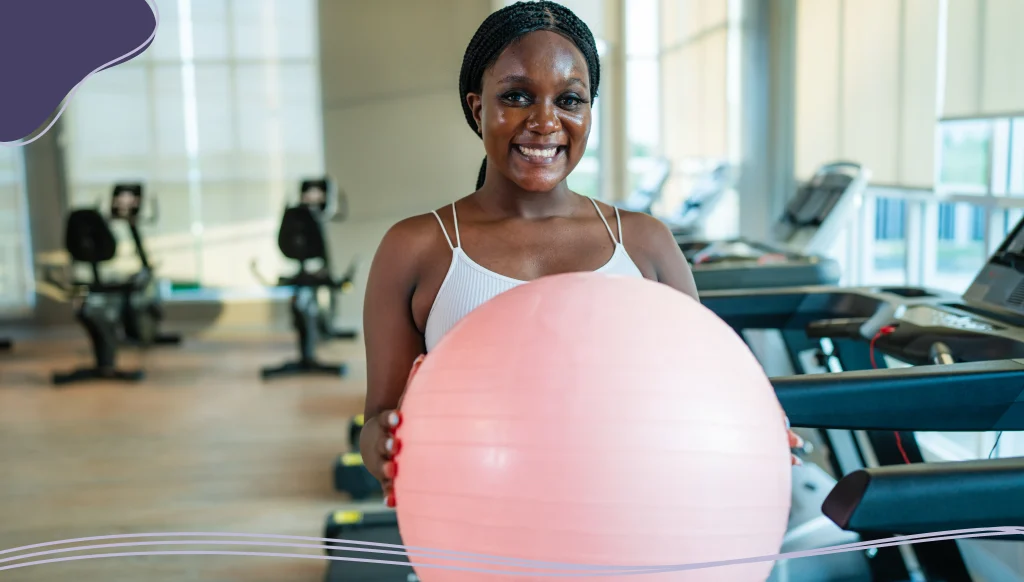 Woman at a gym holding a pink exercise ball
