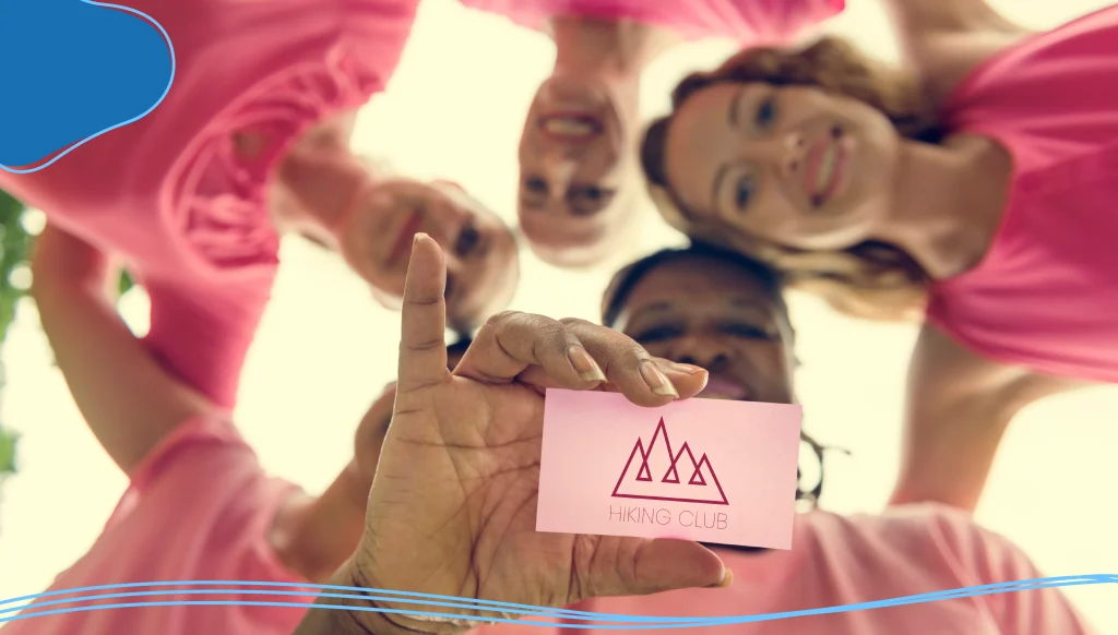 Women wearing pink shirts holding a business card with a pink logo