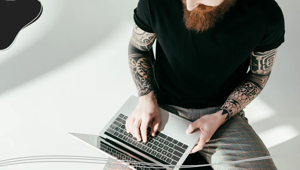 Bearded tattooed man sitting on chair with laptop