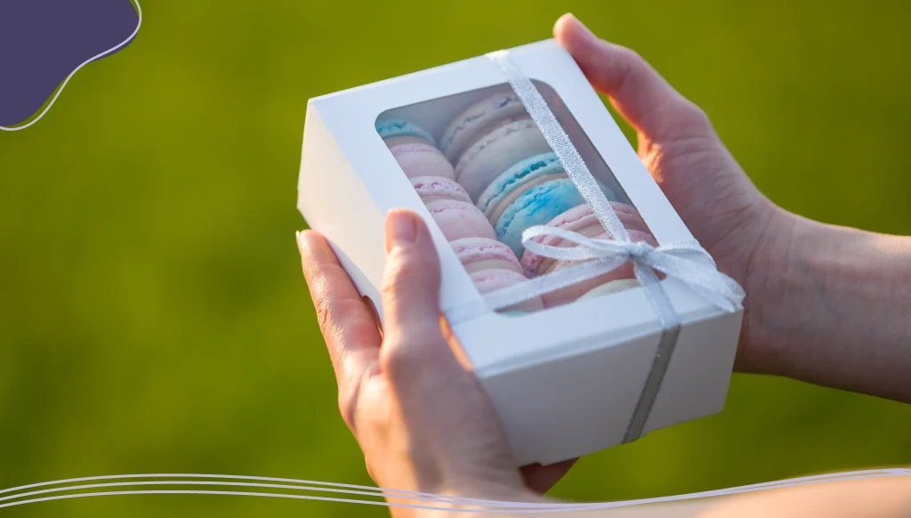 Female hands holding cardboard gift box with colorful pink blue handmade macaron