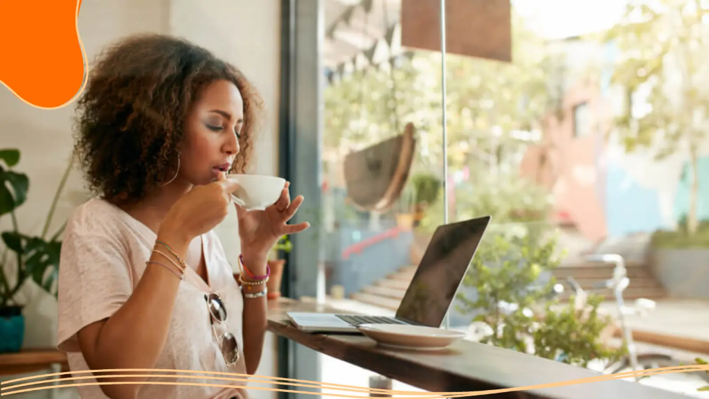 A young woman sips coffee while taking a break from designing a logo to build her brand online.