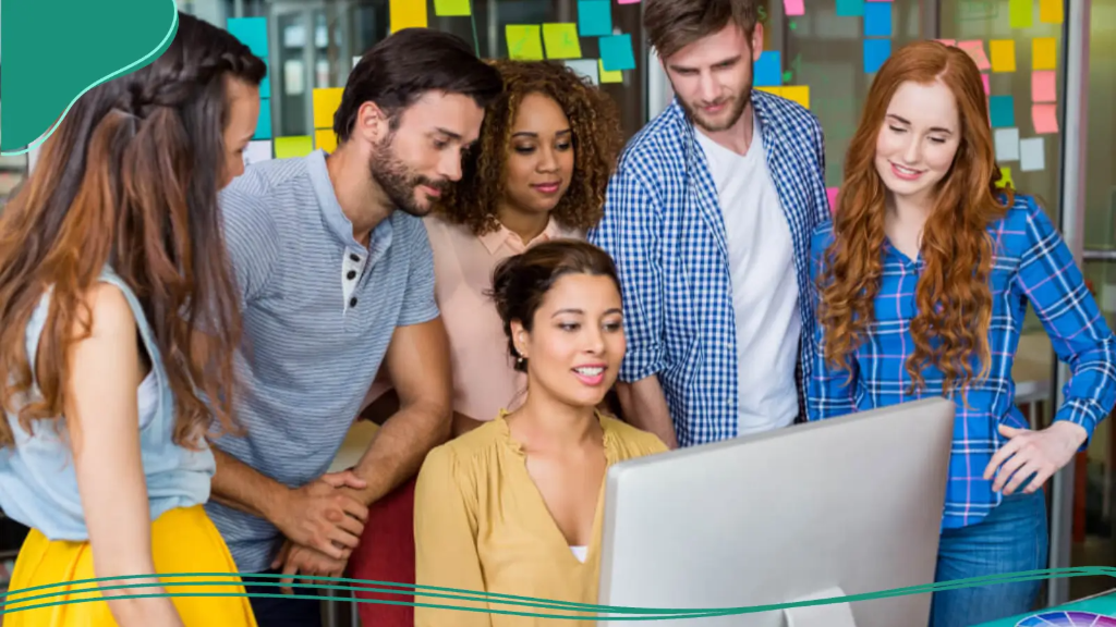 A team of office workers gathers around a desktop computer reviewing their website that has a custom brand online.