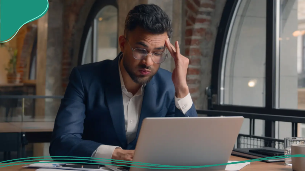 A man looks frustrated while working on his laptop after a mistake slows his progress with personalized branding online.