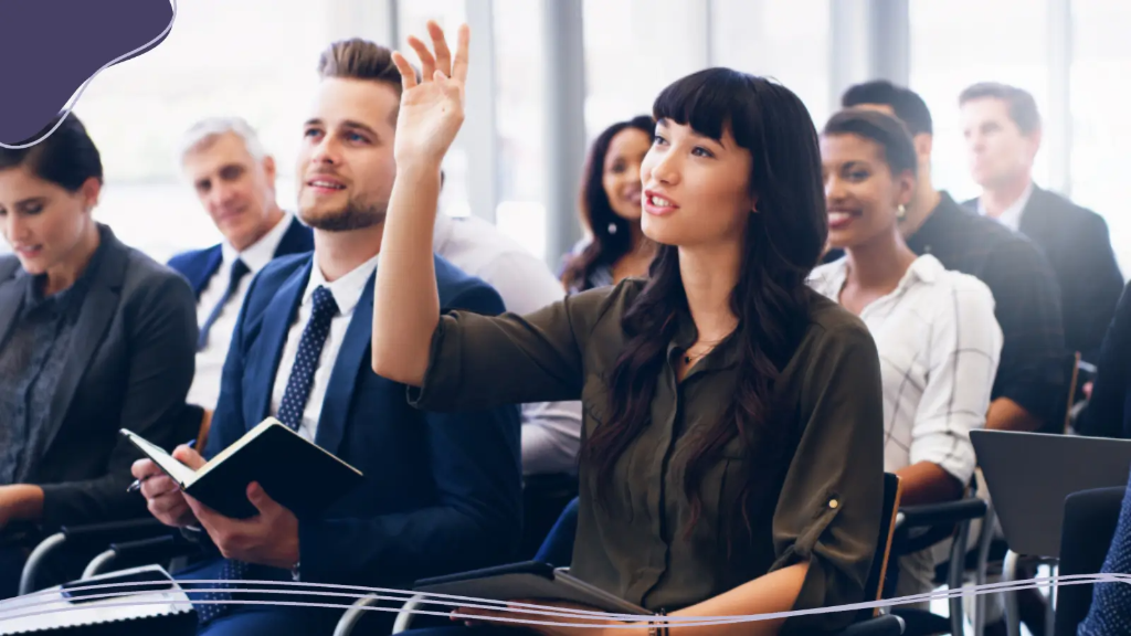 A woman raises her hand to ask a question about using an AI logo maker at a business meeting.