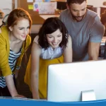 A team of young professionals gather around a computer to choose the best AI tool for logo design.