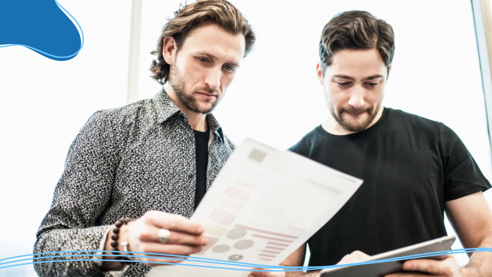 Two men review a one-page brand guide in a brightly lit office, demonstrating how to create your own brand through clear strategy and collaboration.