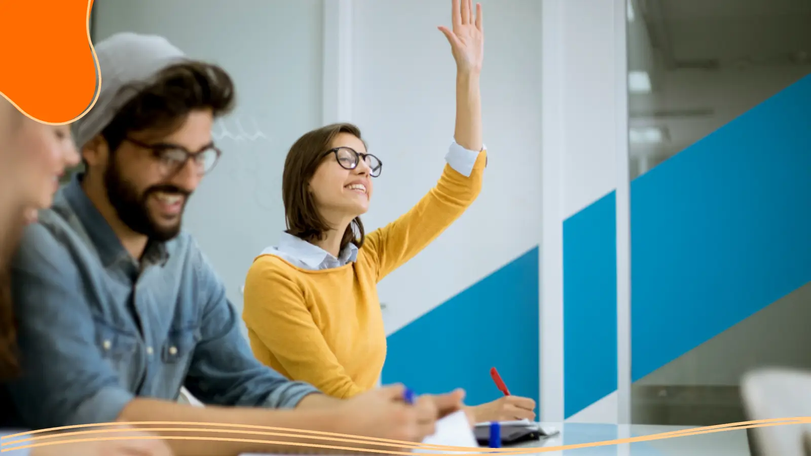 A young woman wearing glasses and a yellow sweater sitting in a modern office, raising her hand with a smile to ask a question while her colleagues sit nearby taking notes, supporting branding for small businesses through active learning and engagement.